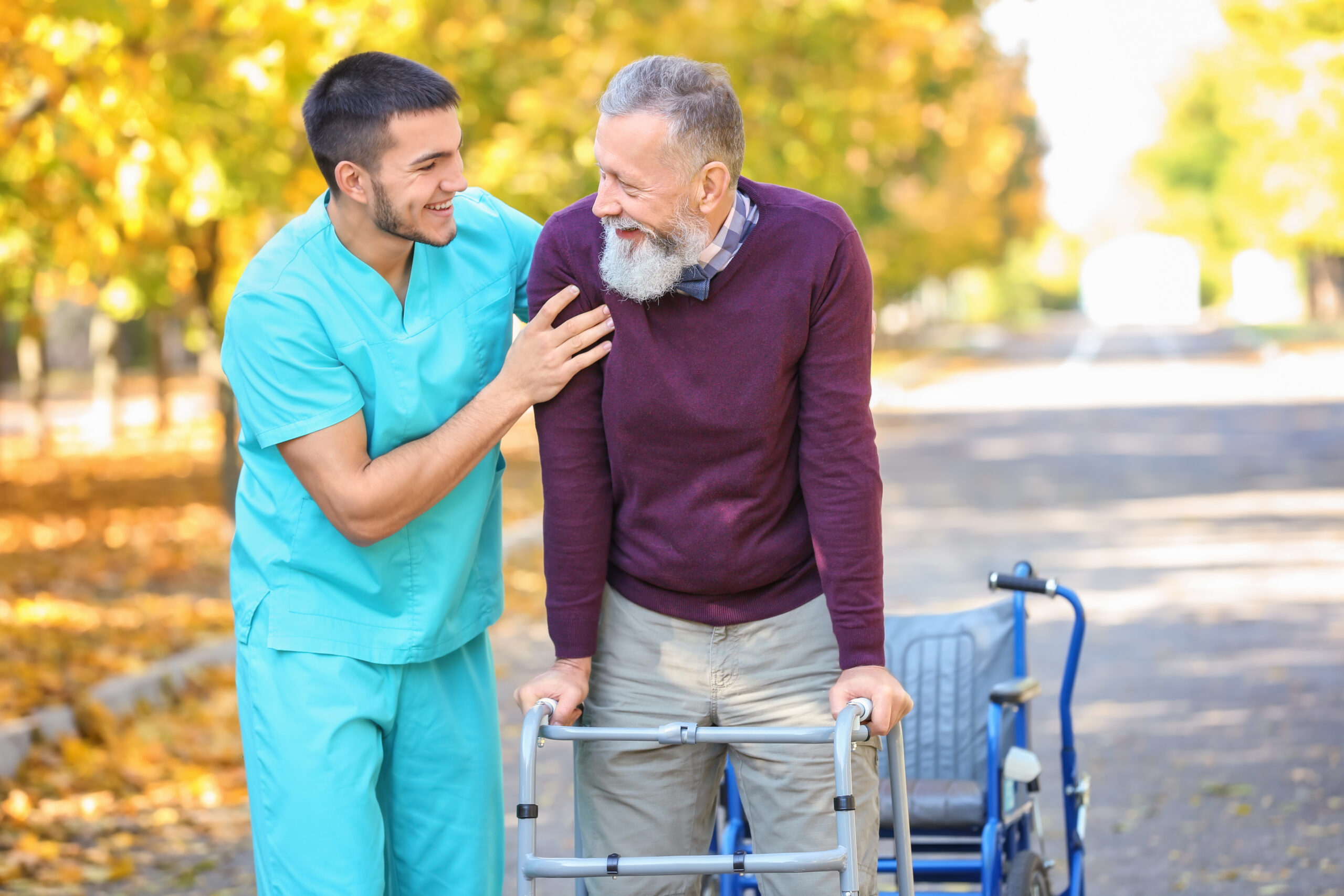 Young caregiver walking with senior man in park