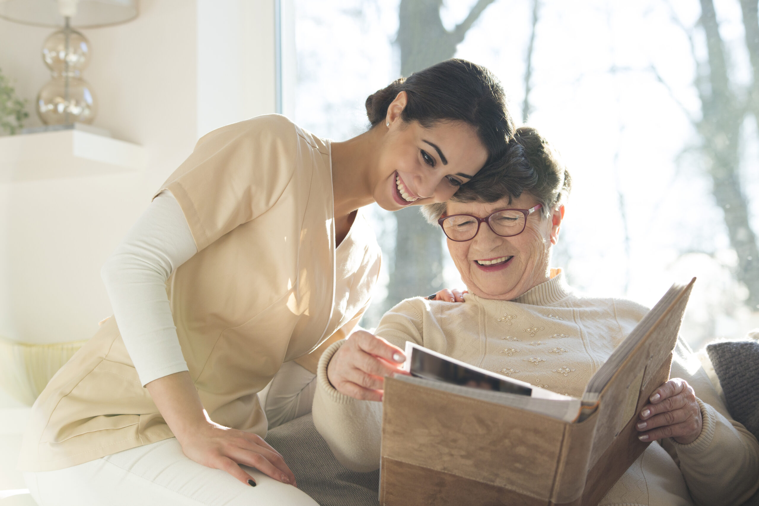 Smiling senior woman watching photo album with happy caregiver